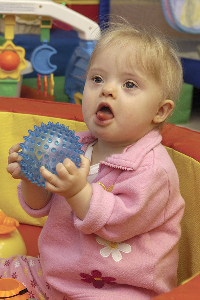 Young girl sitting on the floor in a play area with a blue ball in her hands.