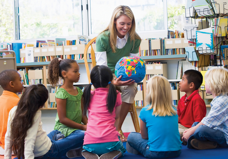 Teacher sitting a chair holding a globe with young students looking on.